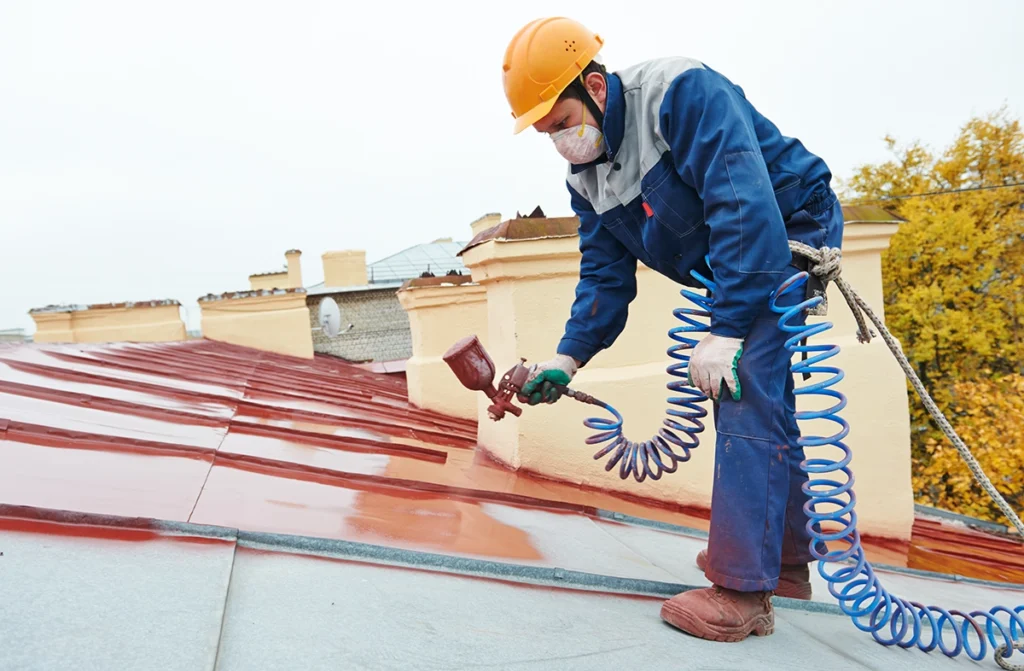 Mężczyzna maluje dach na wysokości.