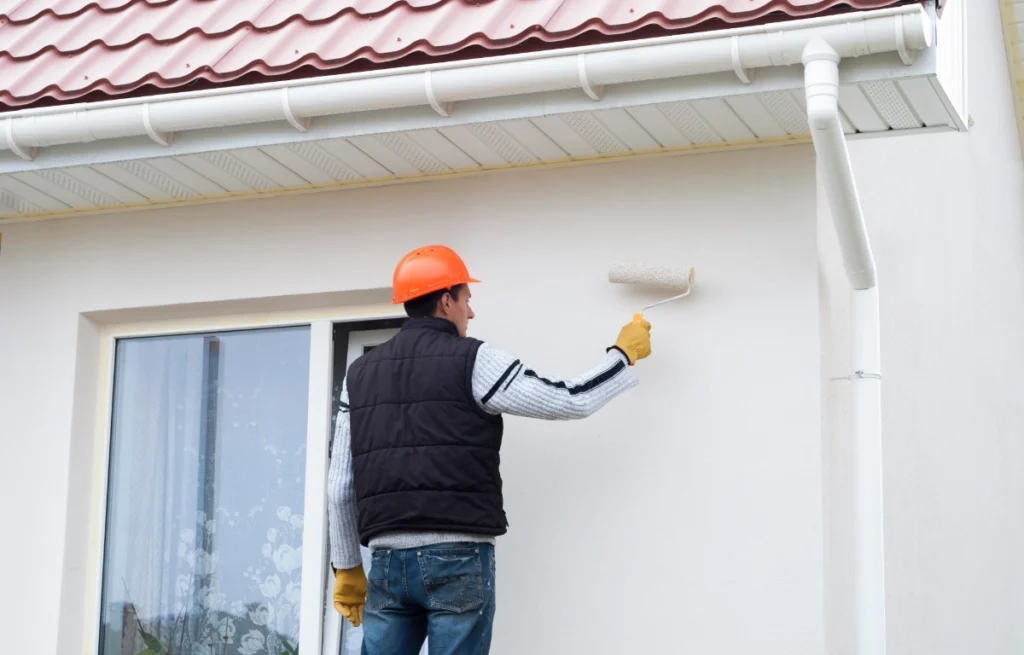 Mężczyzna maluje ścianę domu.